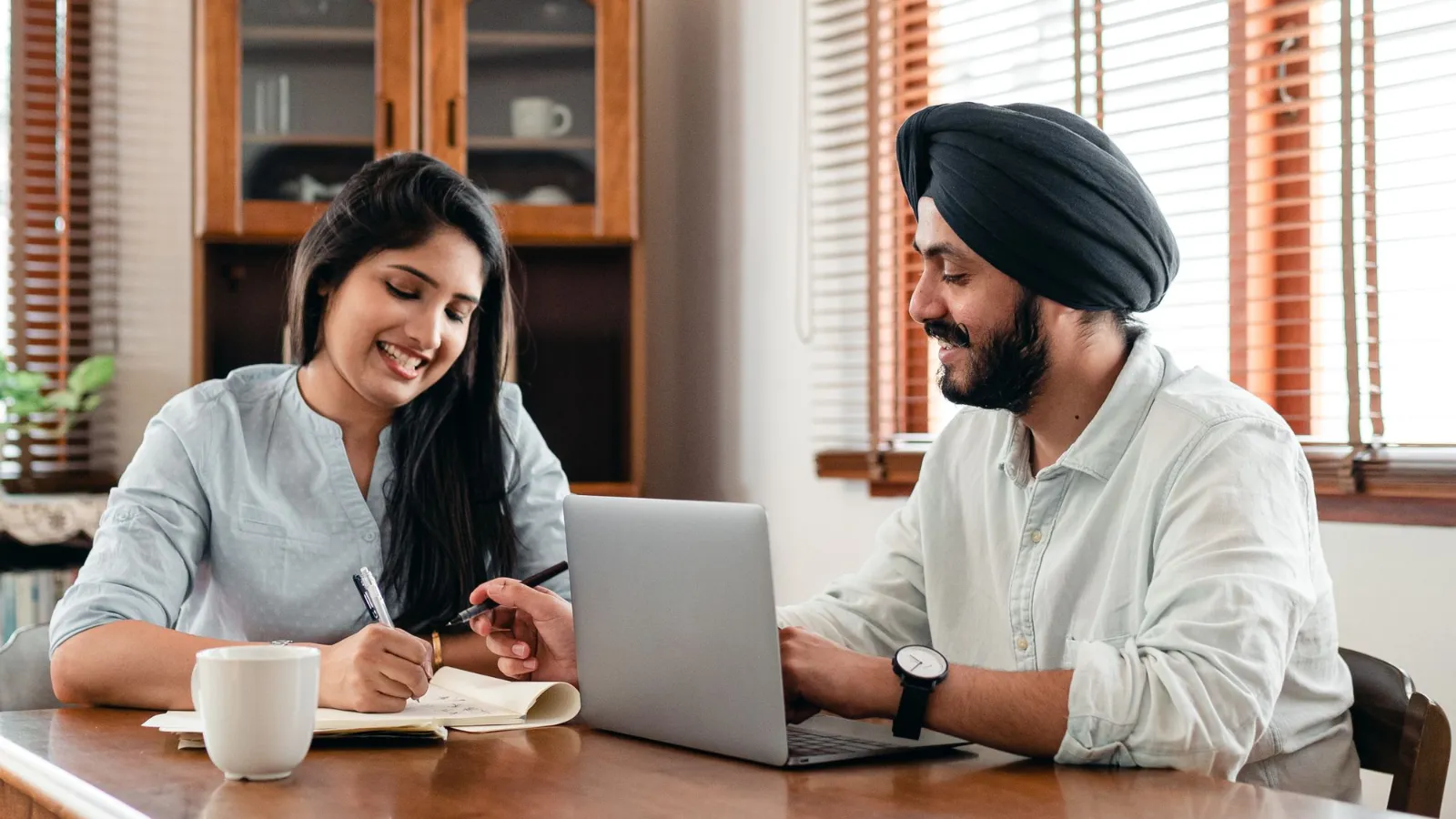 A young Indian man and woman smiling as they work together on a laptop in an office