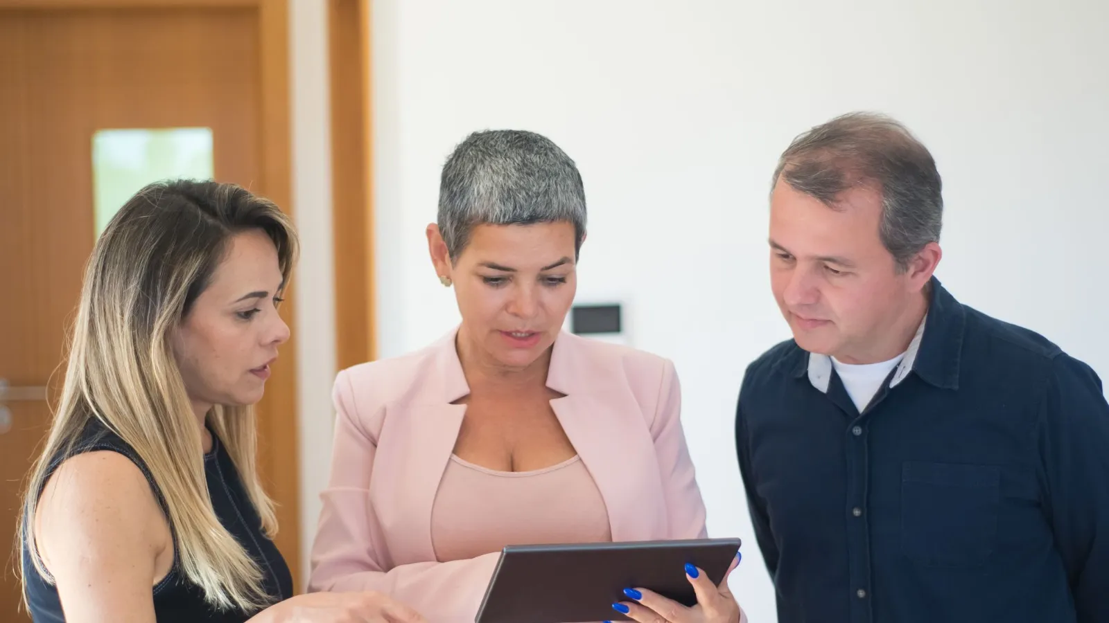 A real estate agent and a couple looking at property options on a digital tablet during a meeting